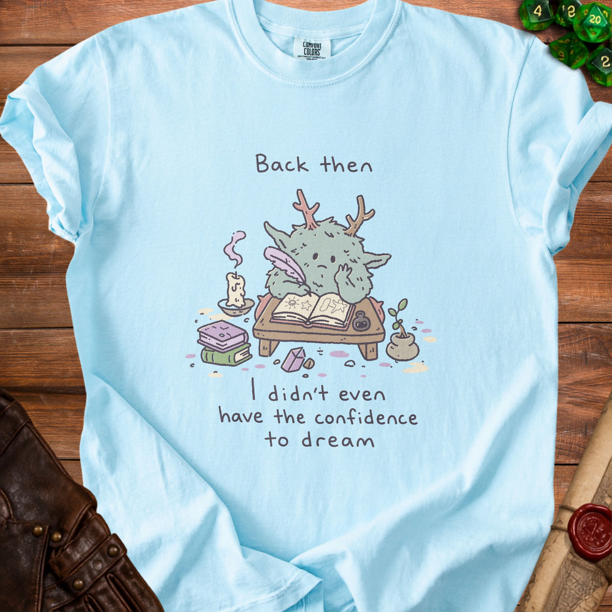 Light blue t-shirt with cartoon monster writing and text "Back then I didn't even have the confidence to dream".
