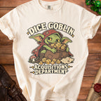 Cream-colored t-shirt featuring a green goblin graphic clutching a bag of dice, with text reading Dice Goblin Acquisitions Department.