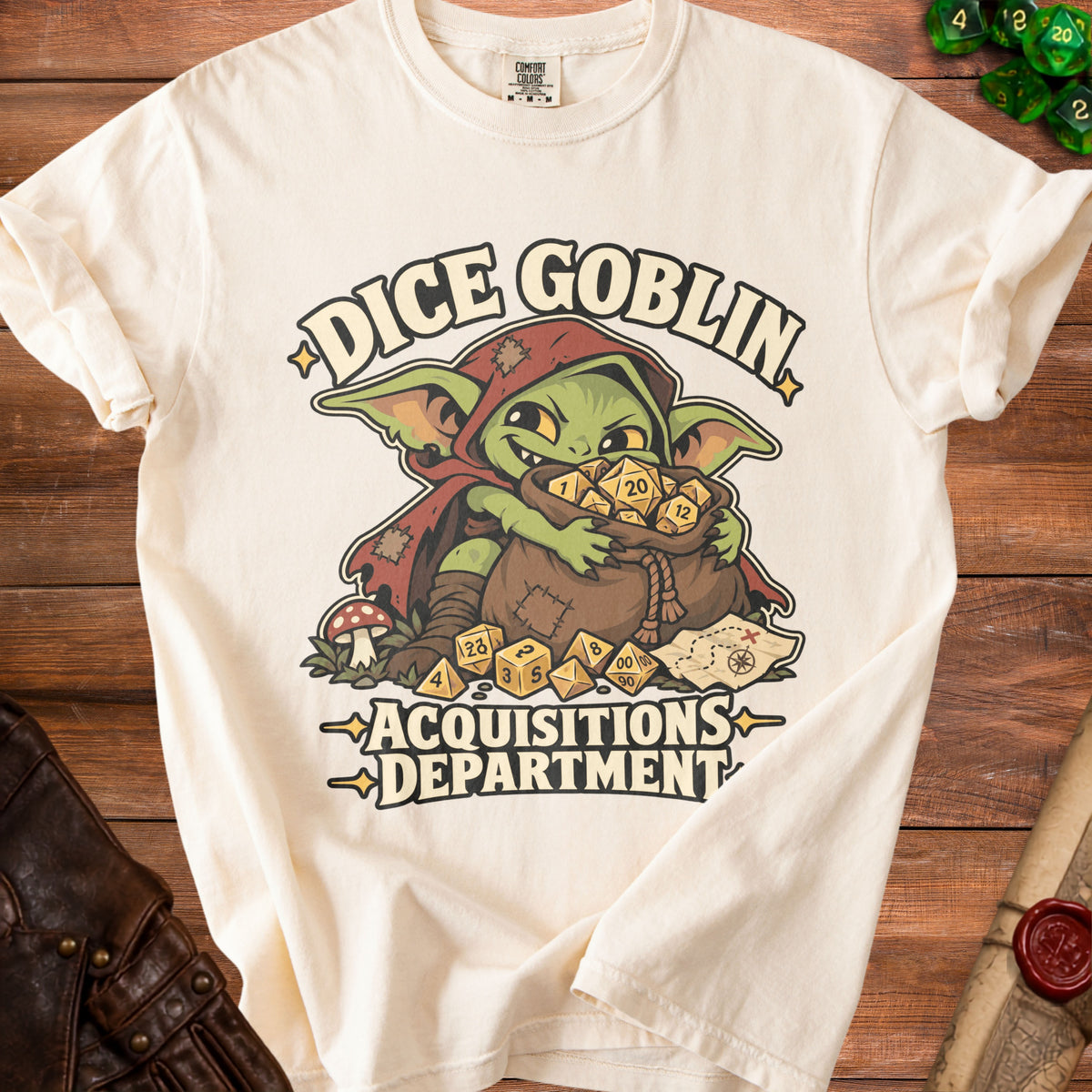 Cream-colored t-shirt featuring a green goblin graphic clutching a bag of dice, with text reading Dice Goblin Acquisitions Department.