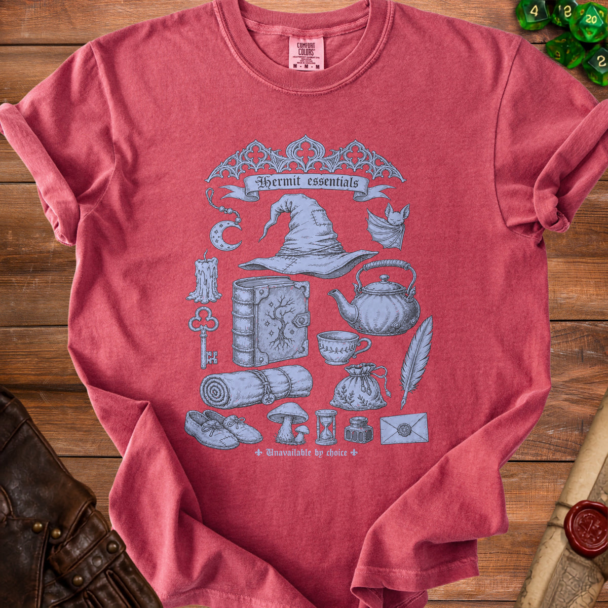 Red t-shirt with "Hermit essentials" and illustrations of magical items, a witch hat, and a bat.