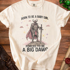 Cream t-shirt with "Born to be a baby girl, forced to be a big dawg" text and warrior graphic.