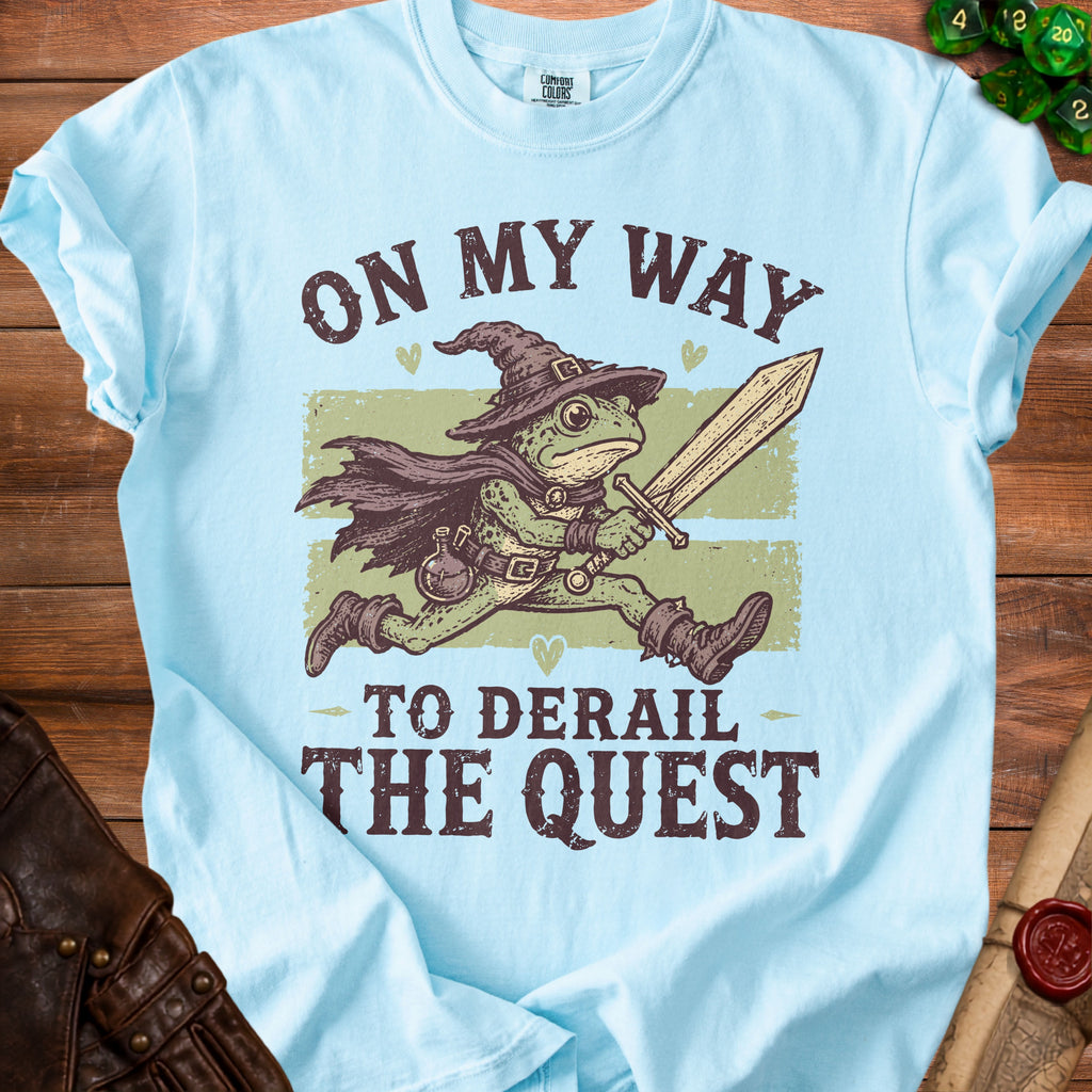 Light blue t-shirt with frog wizard holding a sword and text "ON MY WAY TO DERAIL THE QUEST".