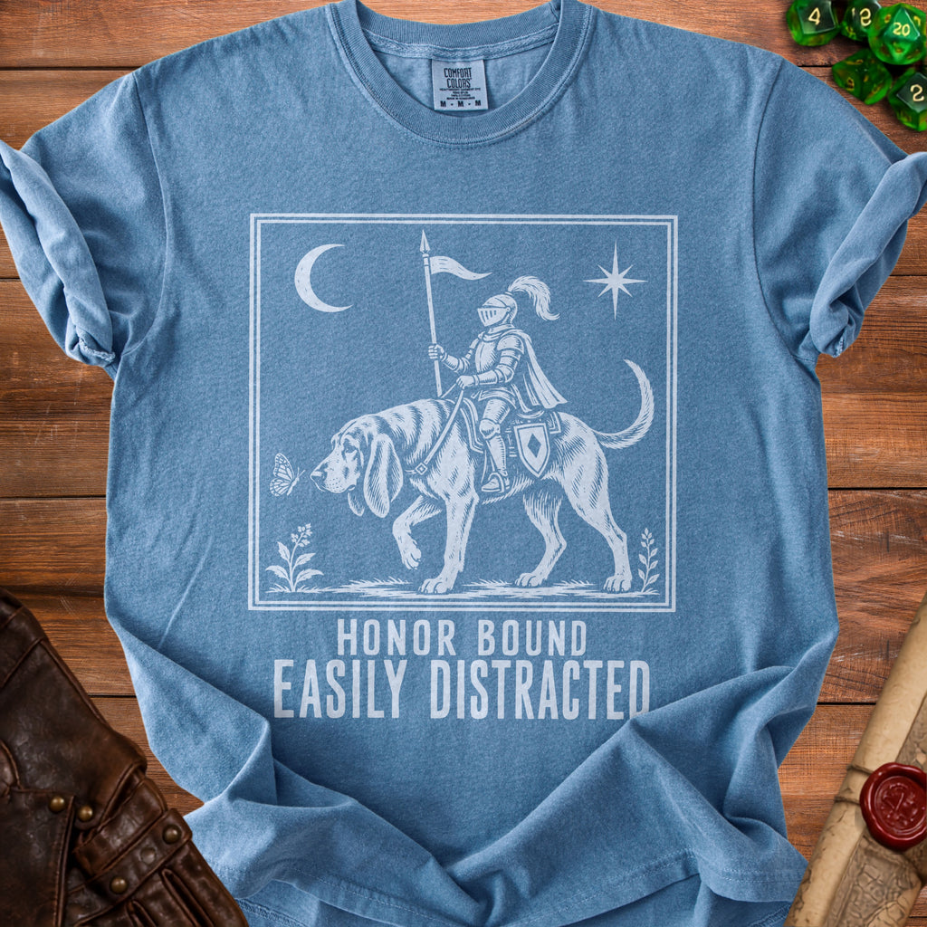 Blue t-shirt with white graphic of knight on dog, crescent moon, star, butterfly, and text "HONOR BOUND EASILY DISTRACTED."