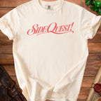 Cream t-shirt with coral "Side Quest!" graphic on wooden background.
