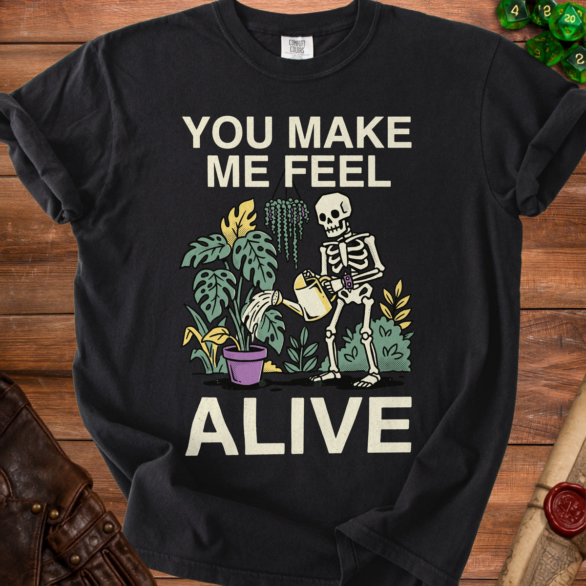 Black t-shirt with skeleton watering plants, text reads "You Make Me Feel Alive"