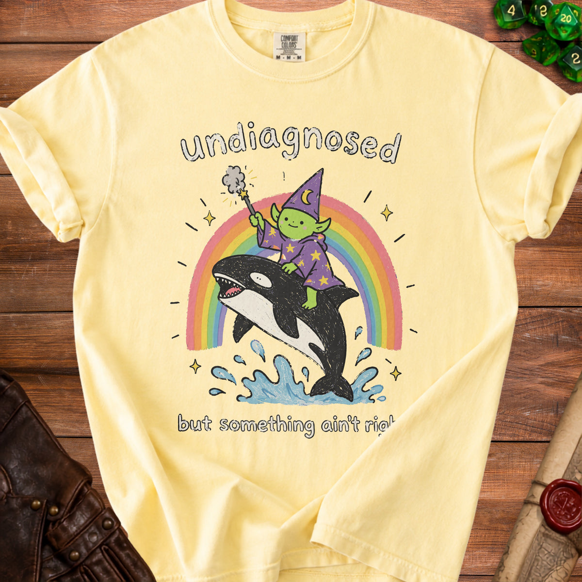 Yellow t-shirt with "undiagnosed but something ain't right" text and wizard riding an orca over a rainbow.