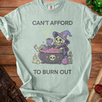 Mint t-shirt with skeleton in cauldron and text "CAN'T AFFORD TO BURN OUT".