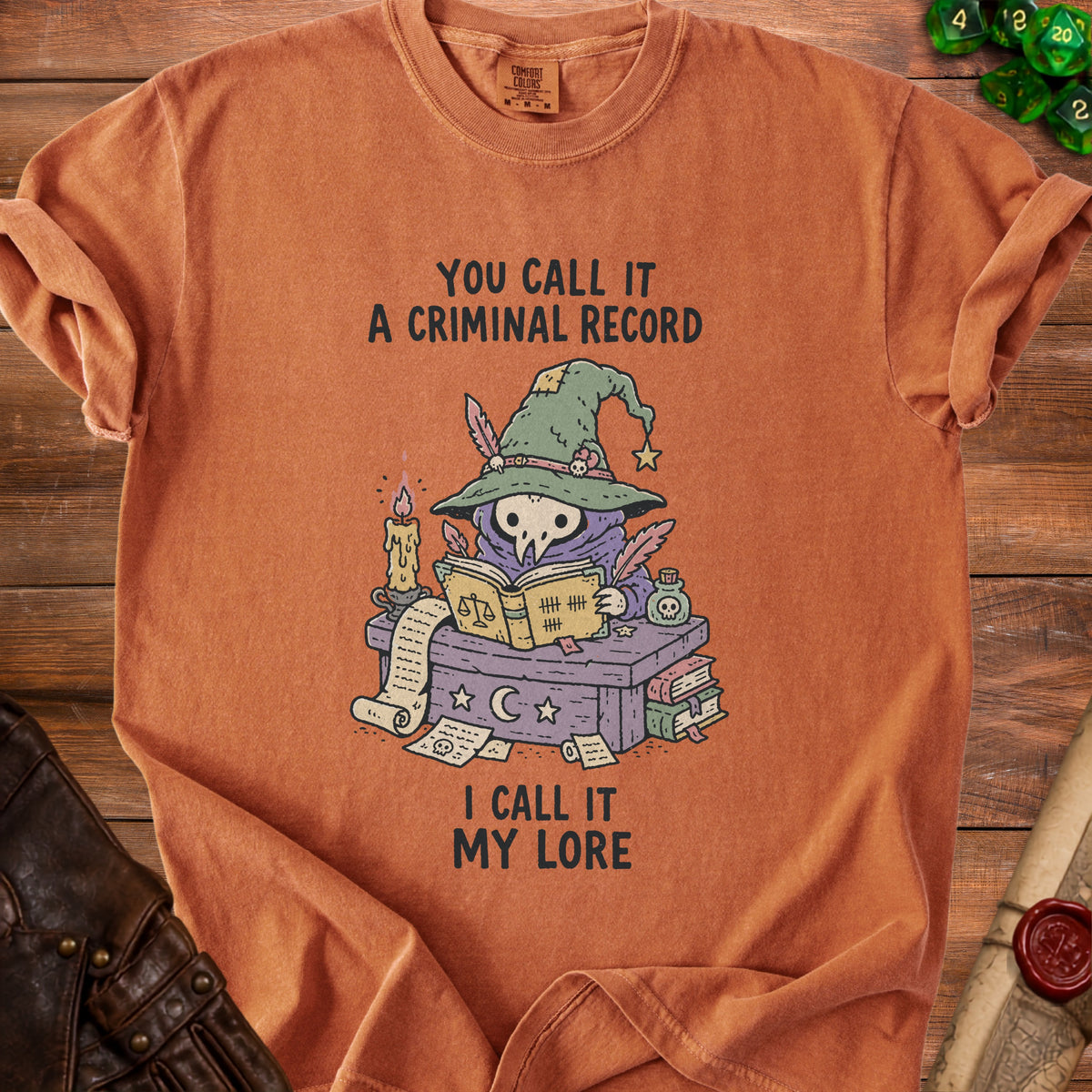 Orange t-shirt with illustration of a skull in a witch hat reading a book.
