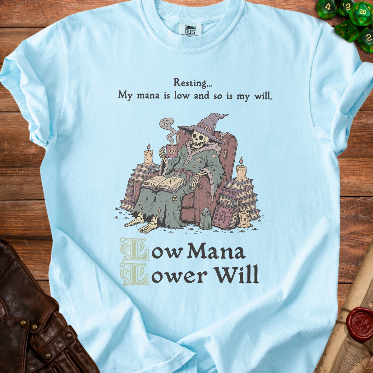 Light blue t-shirt with illustration of a skeleton wizard reading and drinking.