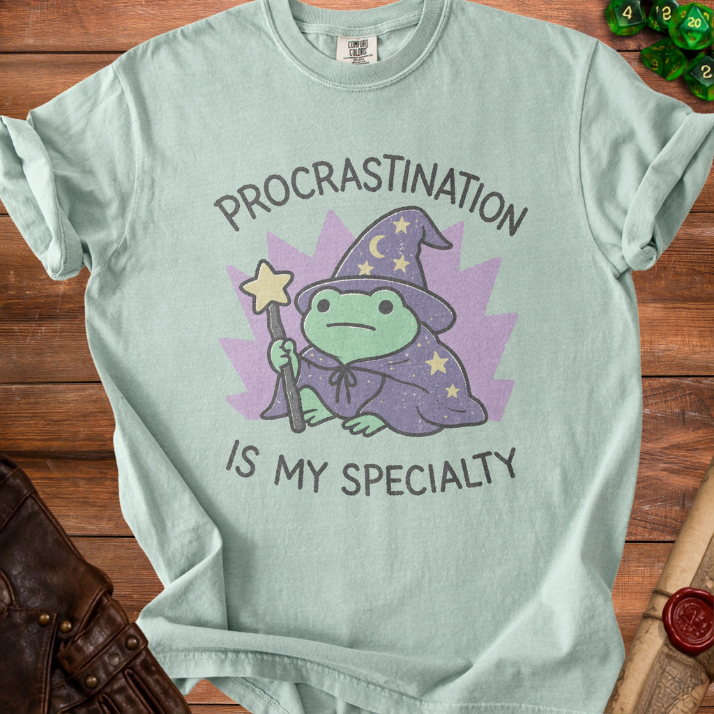 Light blue t-shirt with a frog wizard graphic and text "Procrastination is my specialty."