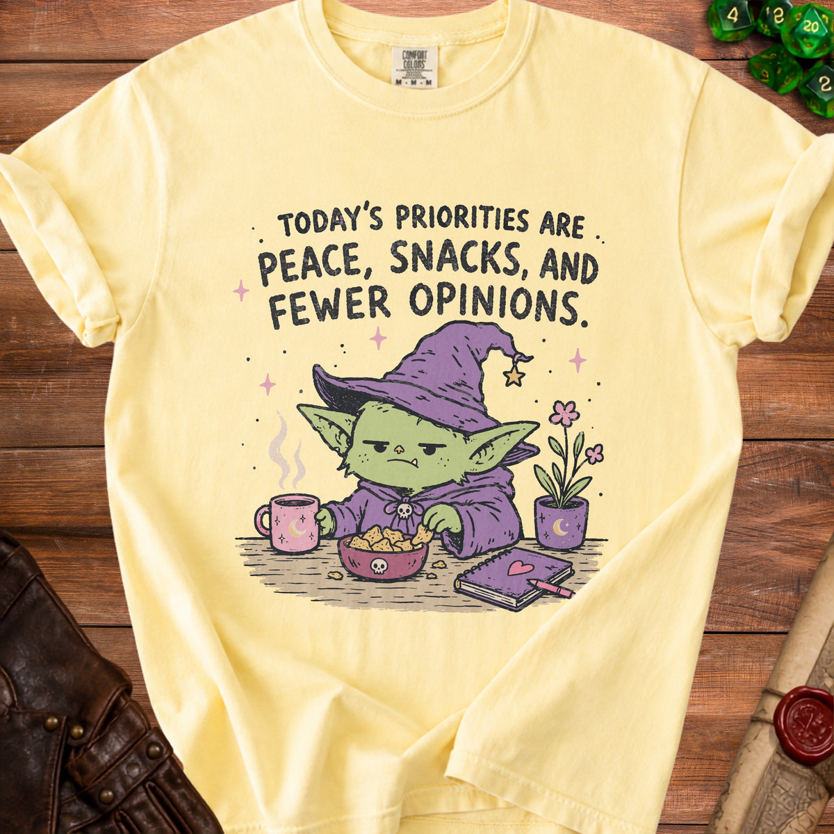Yellow t-shirt with text "Today's priorities are peace, snacks, and fewer opinions" and goblin graphic.