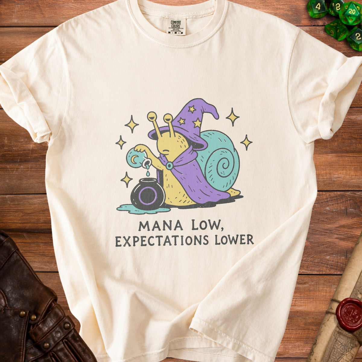 Cream t-shirt with a wizard snail graphic and the text "Mana Low, Expectations Lower".