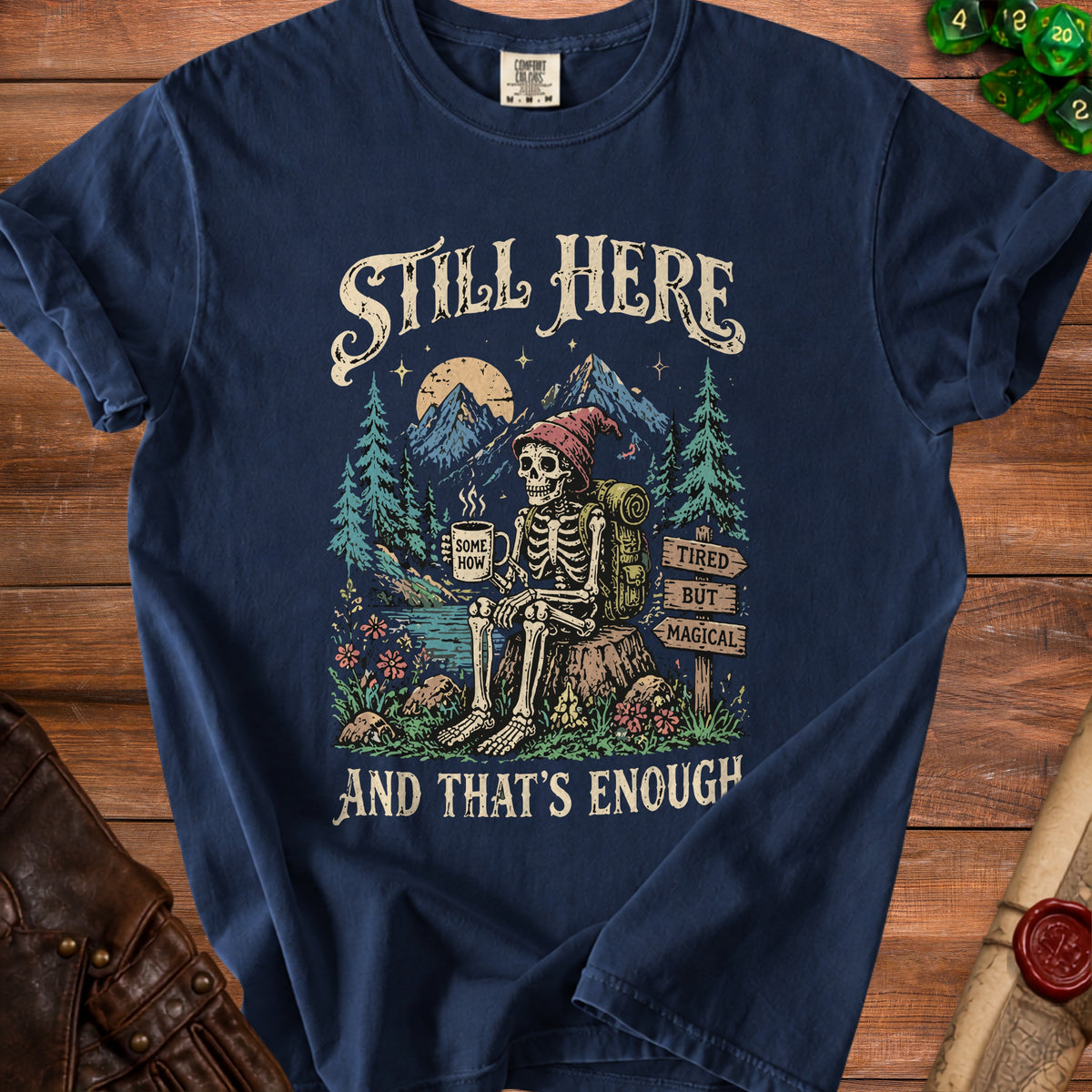 Skeleton hiker with mug in mountain scene, text "Still Here", "Some How", "Tired But Magical", "And That's Enough".