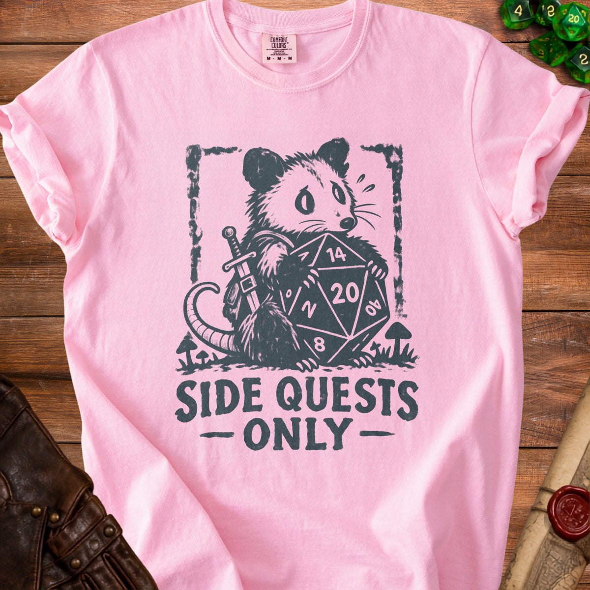 Pink t-shirt with a charcoal graphic of a possum holding a twenty-sided die and sword.