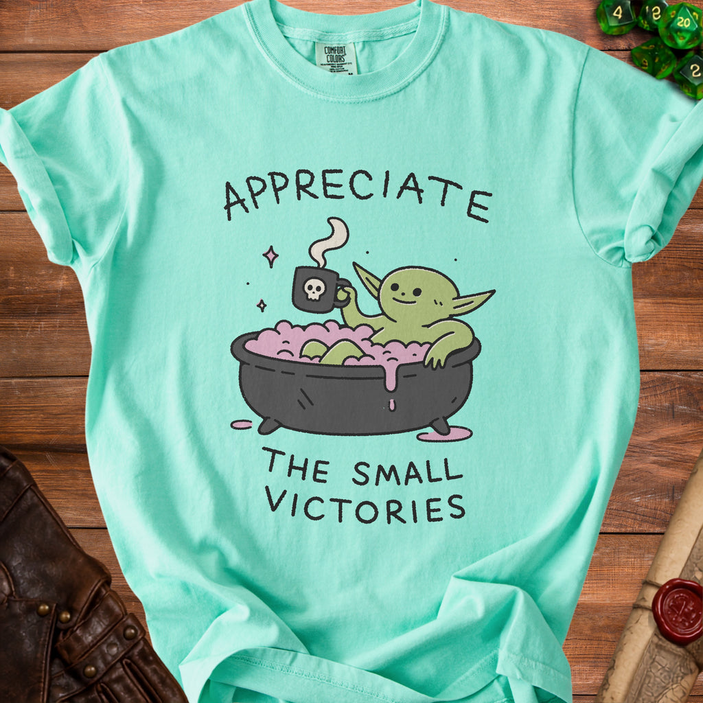 Mint green t-shirt with graphic of creature in bath holding skull mug, text "APPRECIATE THE SMALL VICTORIES".