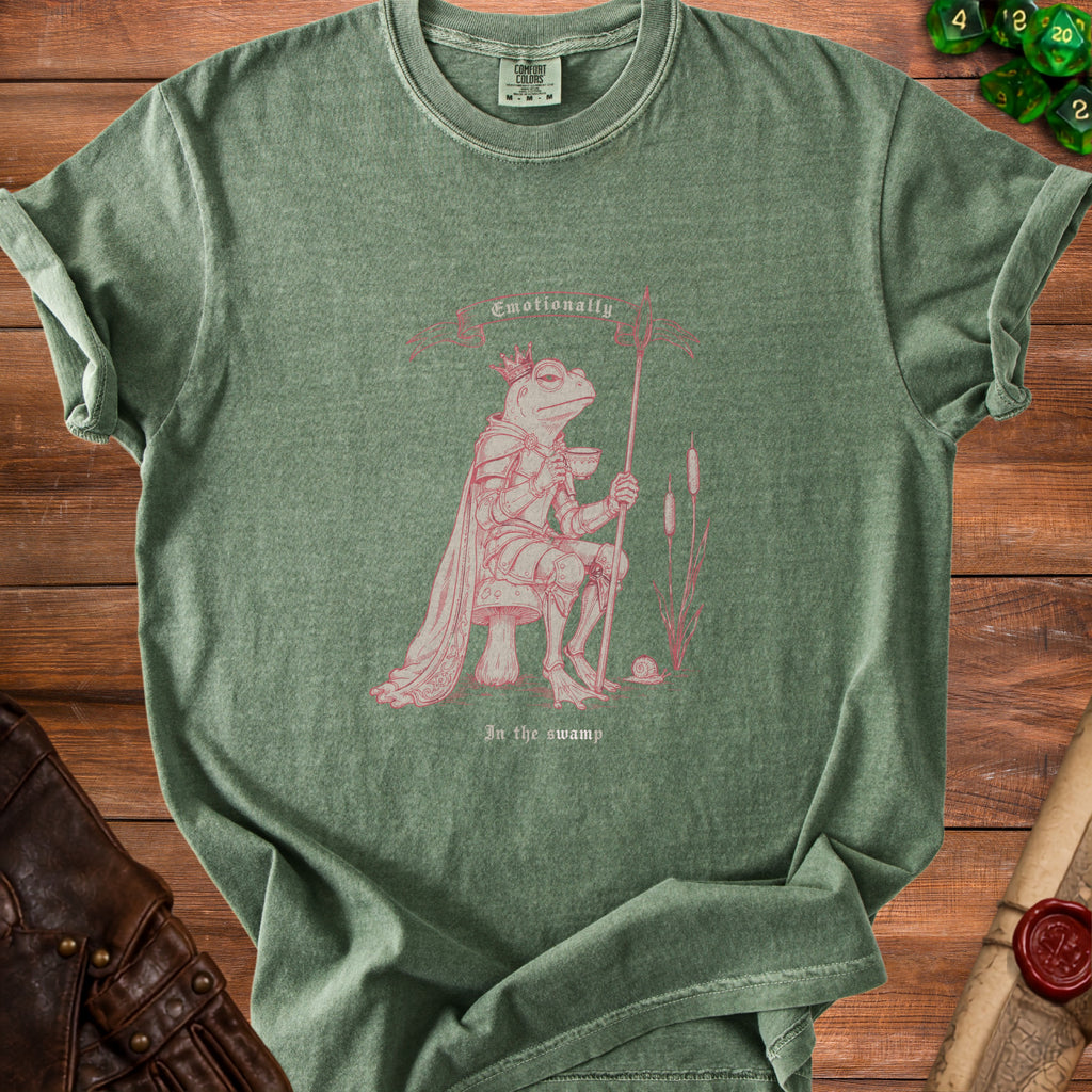 T-shirt with pink illustration of a crowned frog knight holding a cup and spear, text "Emotionally In the swamp".