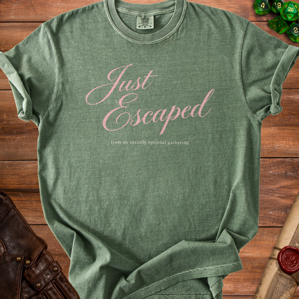 A green t-shirt with pink cursive text reading Just Escaped from an entirely optional gathering.