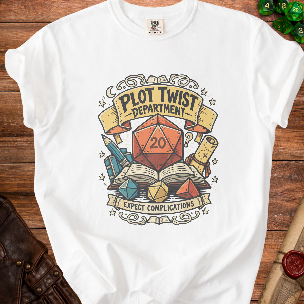 White t-shirt graphic with a d20 die, books, and dice, text reads "Plot Twist Department" and "Expect Complications".