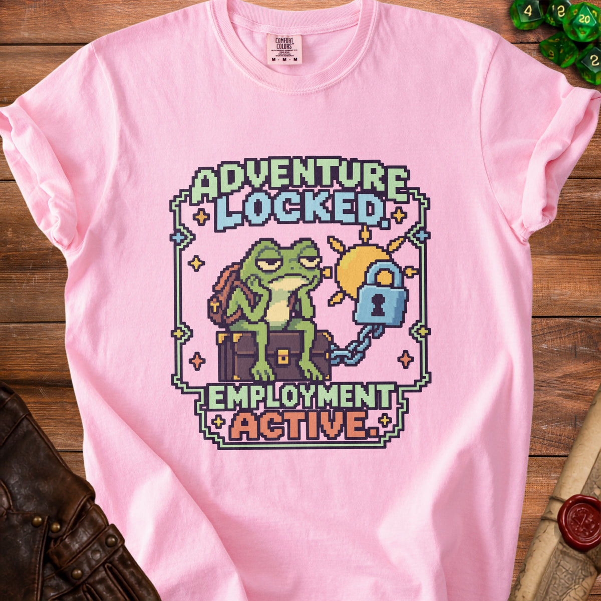 A pink t-shirt featuring pixel art of a bored frog sitting on a locked treasure chest with text reading adventure locked employment active.