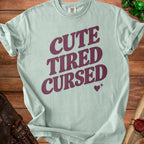 Light green Comfort Colors t-shirt with "CUTE TIRED CURSED" text and a heart.
