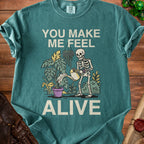 Skeleton watering plants with text "YOU MAKE ME FEEL ALIVE."