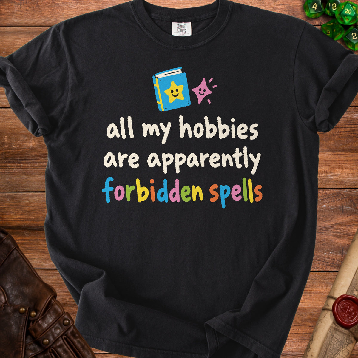Black t-shirt with text "all my hobbies are apparently forbidden spells" and cartoon book.