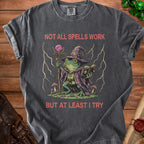 Dark gray t-shirt with wizard frog graphic and text "NOT ALL SPELLS WORK BUT AT LEAST I TRY".