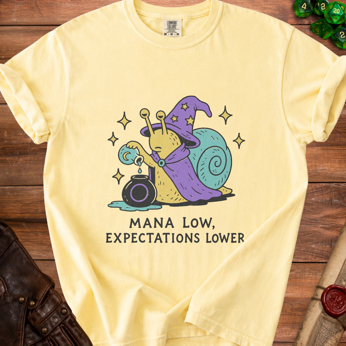 Yellow t-shirt with wizard snail graphic and text "MANA LOW, EXPECTATIONS LOWER".