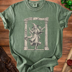 Green t-shirt with graphic of a witch, owl, book, and text "Trying to Maintain Concentration".