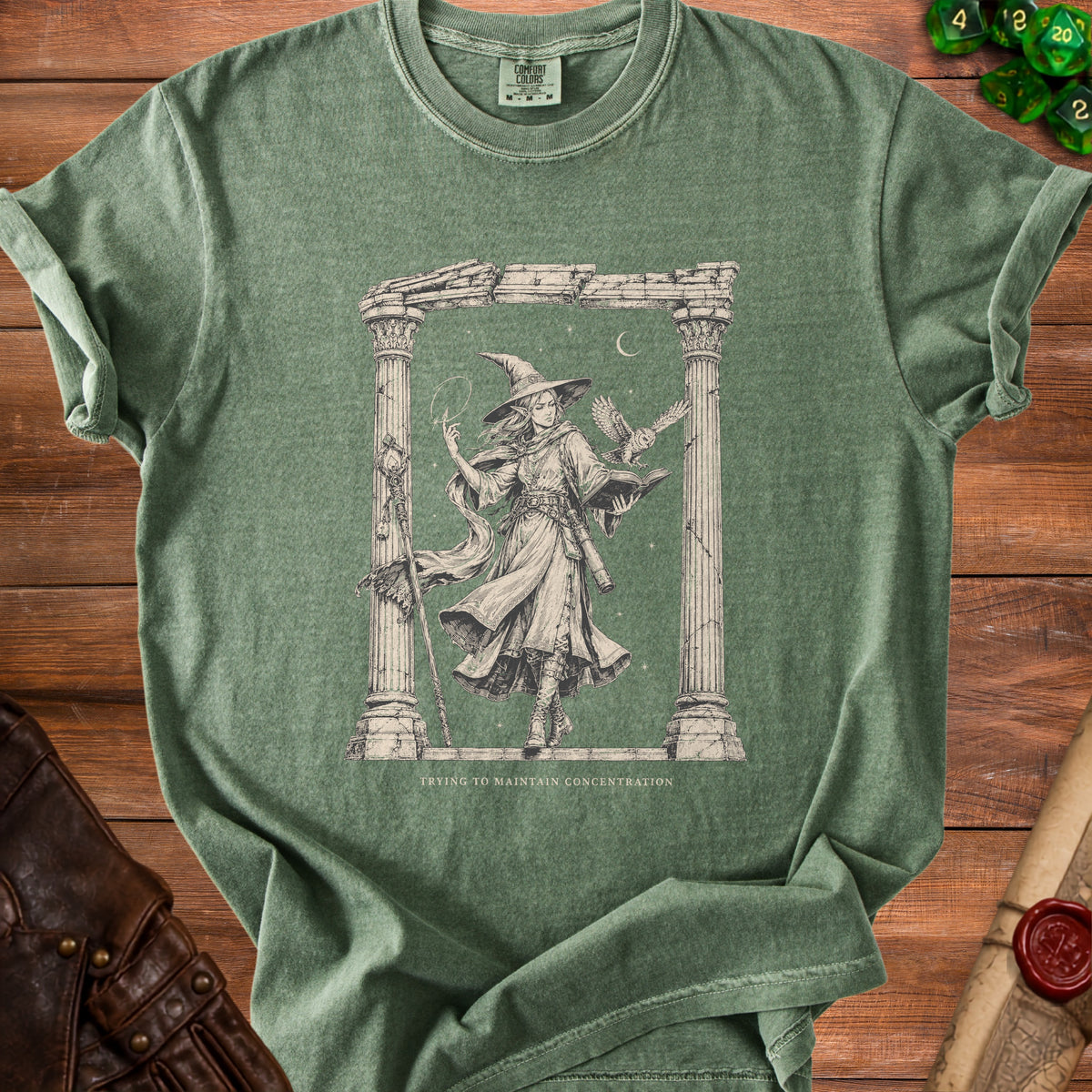Green t-shirt with graphic of a witch, owl, book, and text "Trying to Maintain Concentration".