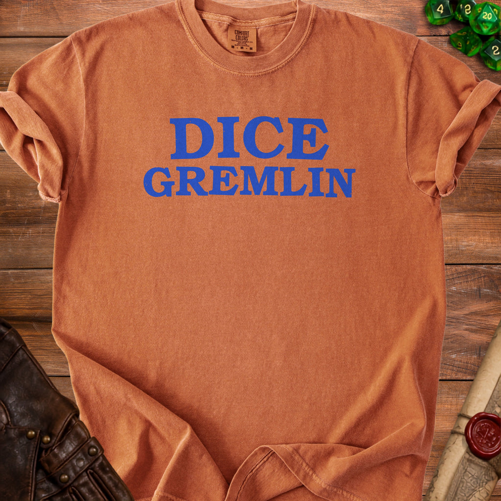 Orange t-shirt with blue text "DICE GREMLIN" on wooden background.