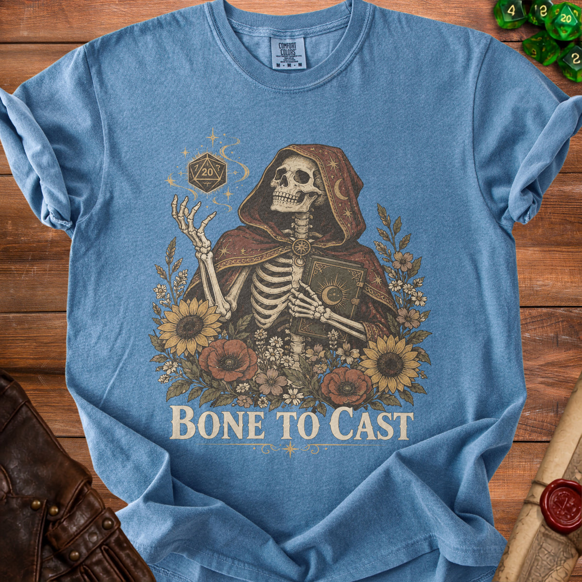 Skeleton in a hooded robe holding a book and a twenty-sided die, with flowers and text "BONE TO CAST."
