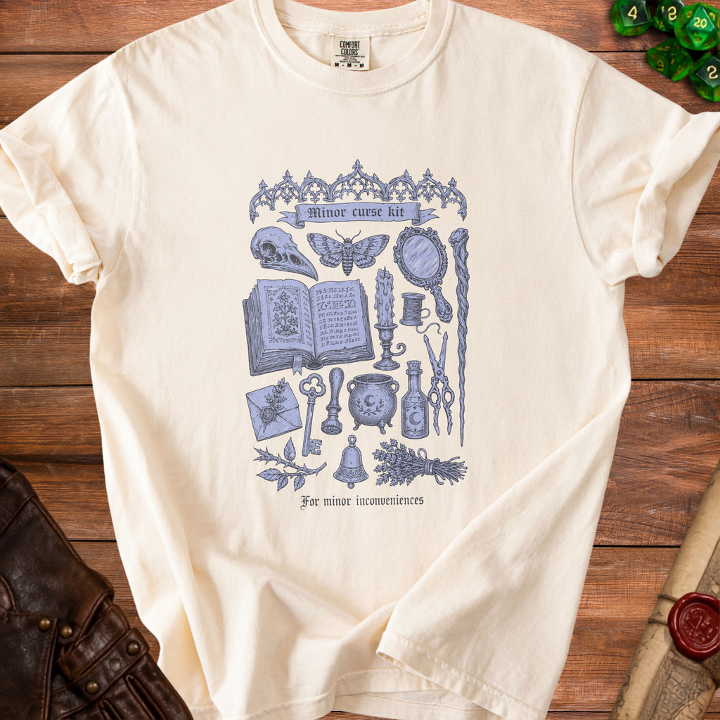 Cream t-shirt with a blue gothic illustration of witchcraft items and the text "Minor curse kit".