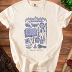 Cream t-shirt with a blue gothic illustration of witchcraft items and the text "Minor curse kit".