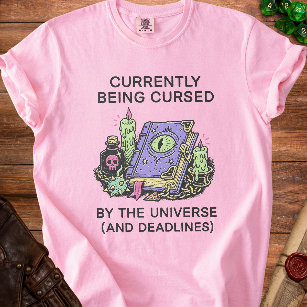 Pink t-shirt with "Currently Being Cursed By The Universe (And Deadlines)" text and a magic book.