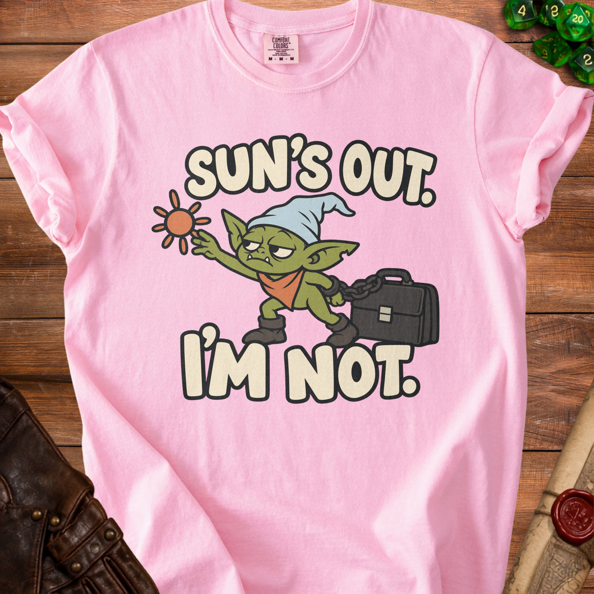 Pink t-shirt with cartoon goblin holding sun and briefcase, text "Sun's Out. I'm Not."