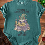 T-shirt with illustration of a skeletal figure in a witch hat reading a book. Text reads "You call it a criminal record. I call it my lore."