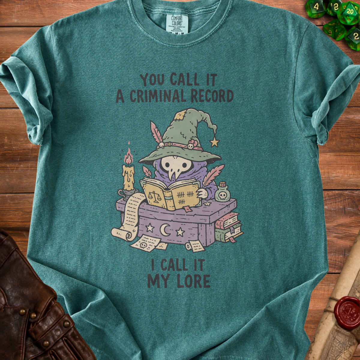 T-shirt with illustration of a skeletal figure in a witch hat reading a book. Text reads "You call it a criminal record. I call it my lore."