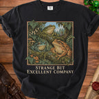 T-shirt with three frogs, ferns, mushrooms, and text "STRANGE BUT EXCELLENT COMPANY".