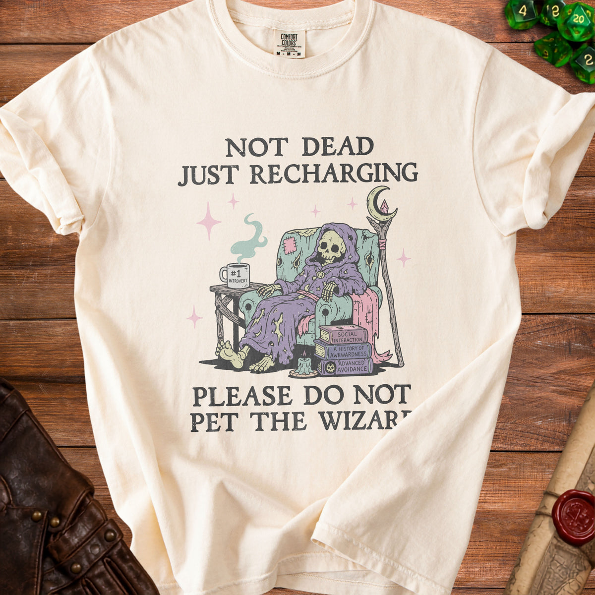Cream t-shirt with "Not Dead Just Recharging" and a skeleton wizard graphic.