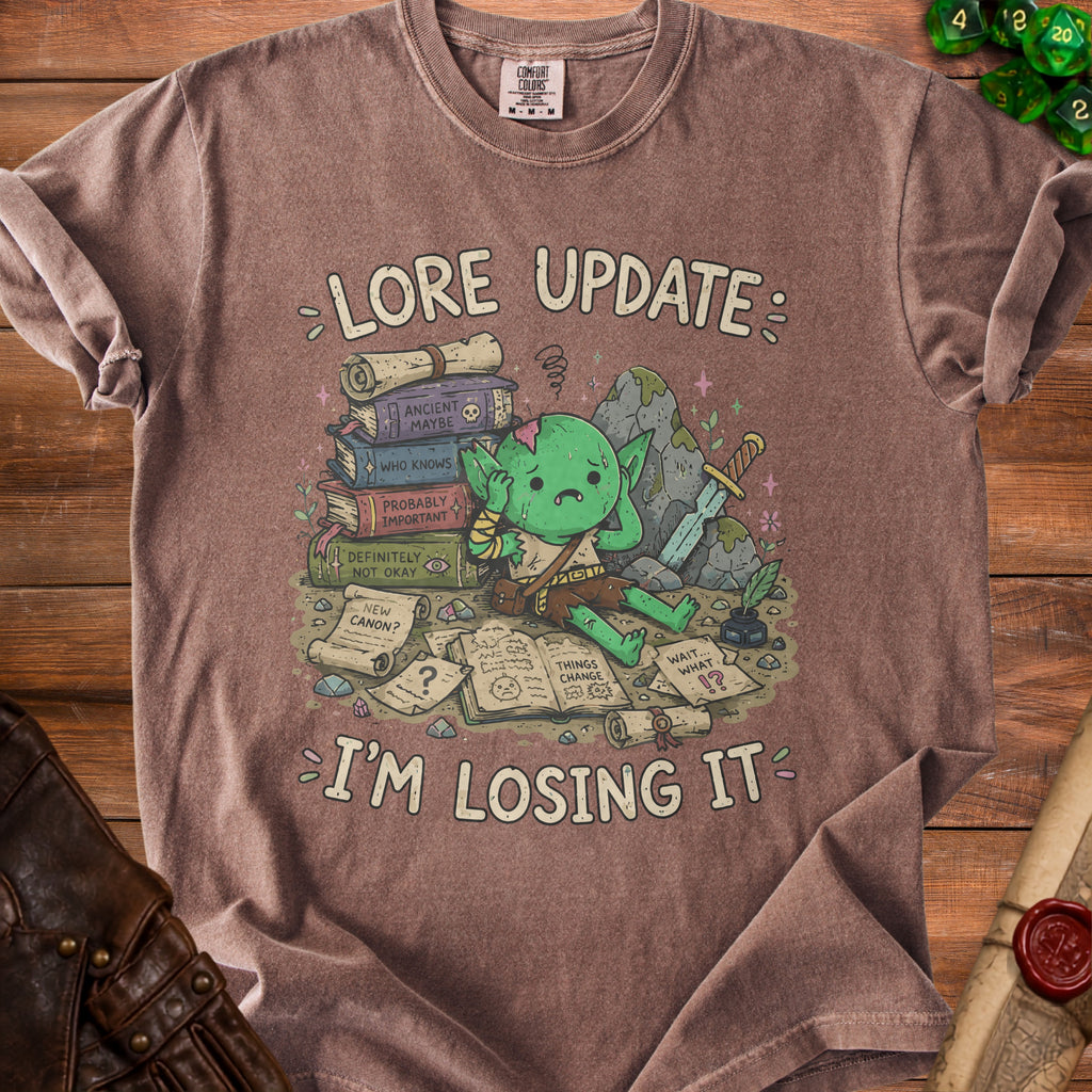 T-shirt with a stressed goblin surrounded by books and scrolls that read "Lore Update: I'm Losing It".
