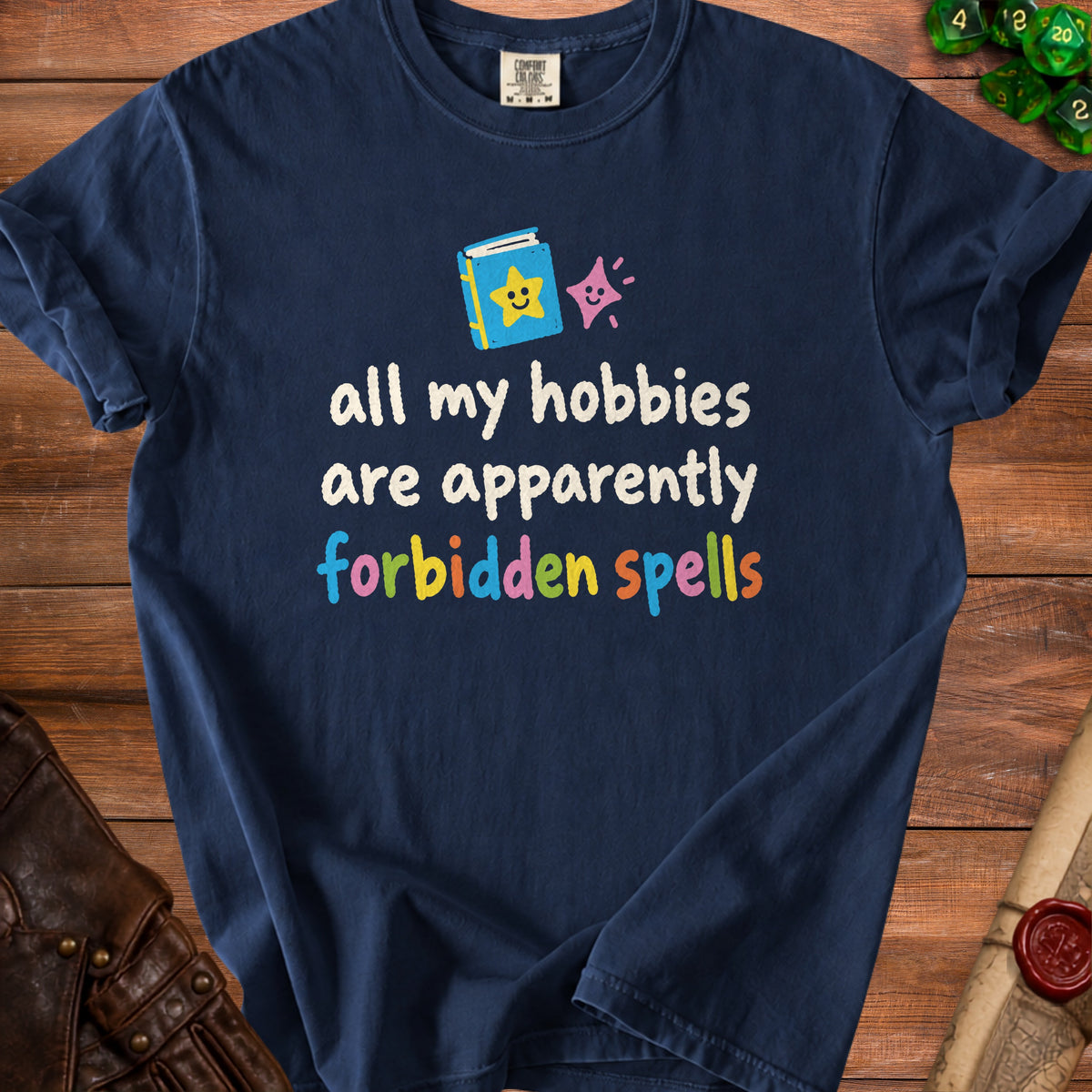 Navy t-shirt with "all my hobbies are apparently forbidden spells" text and book graphic.