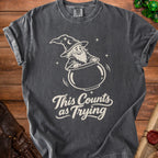 Dark gray t-shirt with white graphic of a wizard and text "This Counts as Trying".