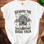 White t-shirt with "Beware the Baba Yaga" text and a spooky house on chicken legs.