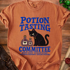 Orange t-shirt with black cat, potion bottles, and "Potion Tasting Committee" text.