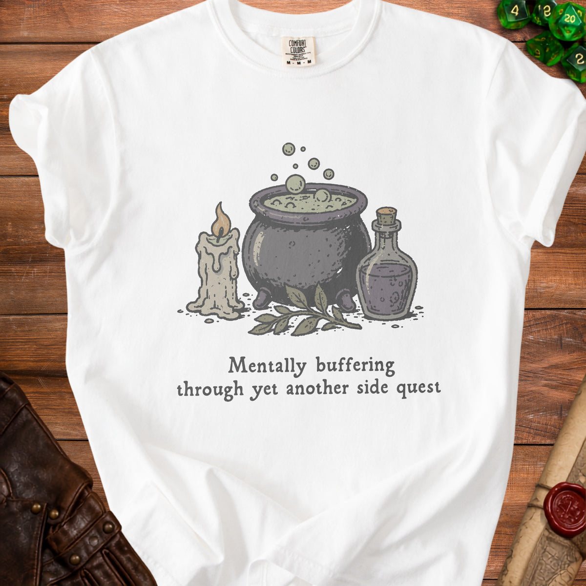 White t-shirt with illustration of cauldron, candle, bottle, and text "Mentally buffering through yet another side quest".