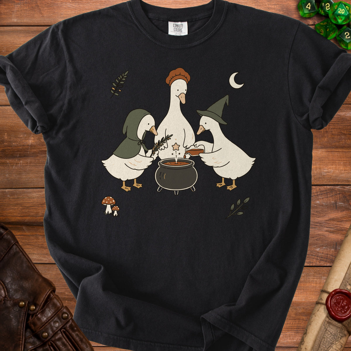Black t-shirt featuring a graphic of three cartoon ducks wearing witch hats brewing a potion.