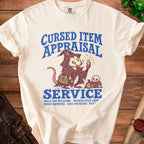 Cream t-shirt with blue text and graphic of a possum in wizard attire appraising a gem.