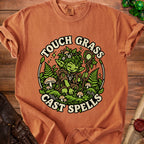 Brown t-shirt with green goblin graphic saying "Touch Grass Cast Spells".