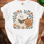 White t-shirt with a cartoon ghost reading a book next to a pumpkin.